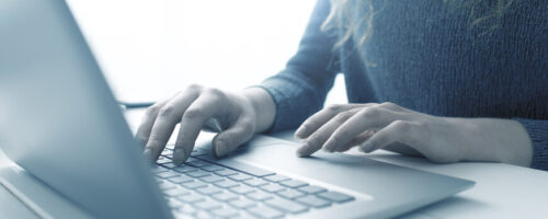 A person types on a laptop, with just their hands showing